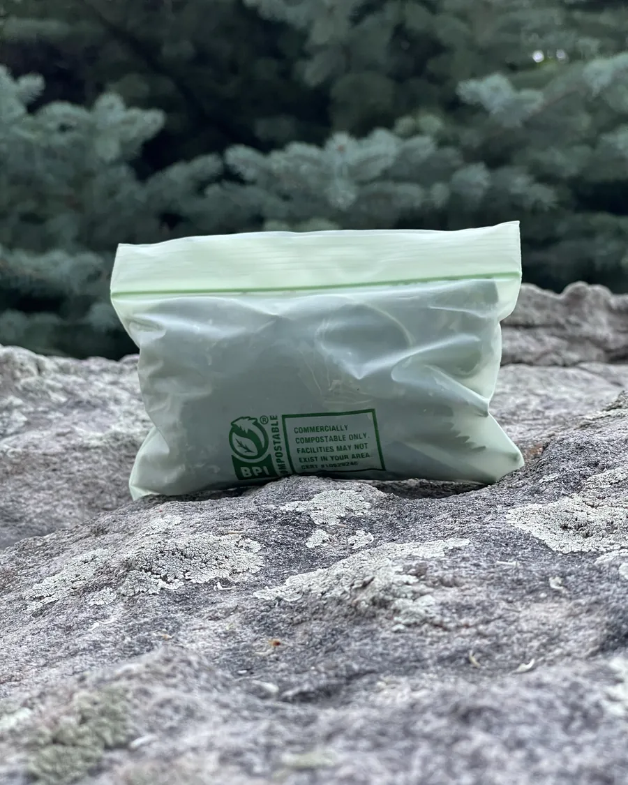 A one ounce bag of Cowboy Catnip fresh catnip standing on a boulder in front of evergreens